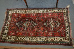 A small Persian rug, red ground with stylised decoration, 132cm x 77cm.