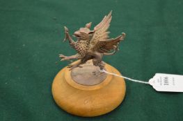 A cast silver model of a dragon mounted on a wooden base.