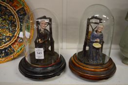 An amusing pair of elderly figures seated on chairs, housed under glass domes.