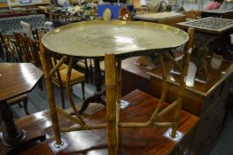 An engraved brass circular tray on folding bamboo stand.