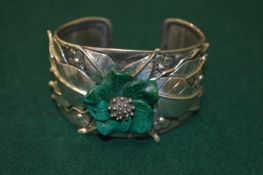 A silver bangle set with a hard stone flower.