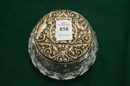 A CUT GLASS DRESSING TABLE JAR with embossed silver cover.