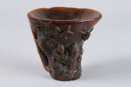 A CHINESE CARVED HORN LIBATION CUP, the sides carved with figures and almond blossom. 6ins high.