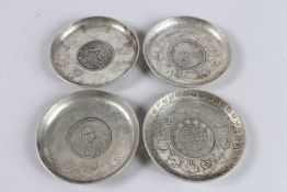 FOUR VARIOUS CHINESE WHITE METAL COIN DISHES, set with various coins and motifs. 3.75ins diameter.