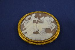 A yellow metal mounted cameo depicting a horse drawn chariot.