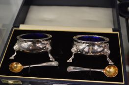 A cased pair of silver circular salts with blue glass liners, London 1991.