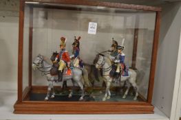 A set of four military figures on horseback in a display case.