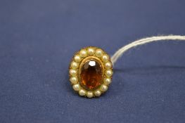A yellow metal dress ring, the central orange coloured stone surrounded by seed pearls.