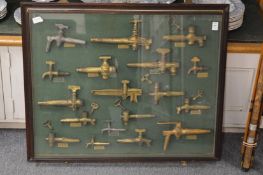 A framed and glazed display of beer keg and similar taps.