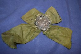 A small embossed silver badge with ribbon.