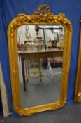 A decorative gilt framed mirror with ribbon cresting, 150cm high x 86cm wide.