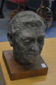 A bronzed composite head of a man on a wooden plinth.