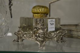 Cut glass inkwell with brass hinged top and ornate cast metal stand.