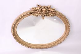 A DECORATIVE FRENCH STYLE GILT FRAMED OVAL WALL MIRROR, with cherub and mask cresting, 3ft 10in wide