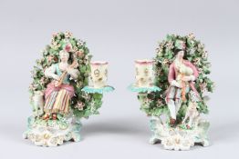 A PAIR OF 19TH CENTURY CHELSEA DERBY BOCAGE FIGURAL CANDLESTICKS, modelled as a seated male figure