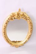 A DECORATIVE FRENCH STYLE GILT FRAMED OVAL WALL MIRROR, with birds and classical trophies