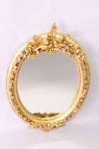A DECORATIVE FRENCH STYLE GILT FRAMED OVAL WALL MIRROR, with birds and classical trophies