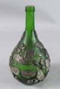 A GREEN GLASS BOTTLE with metal overlaid decoration depicting acorns and oak leaves.