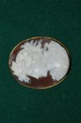 A yellow metal mounted cameo depicting portrait bust of a young lady.
