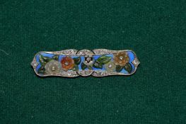 A white metal bar brooch stamped 750 mounted with various gem stones and hard stones.