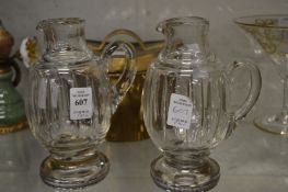 A pair of cut glass jugs with white metal mounts.
