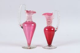 A PAIR OF VICTORIAN RUBY GLASS AND WHITE ENAMEL EWERS. 9ins high.