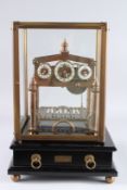 A REPRODUCTION BRASS 'CONGREVE' ROLLING BALL CLOCK, housed in a glass case.