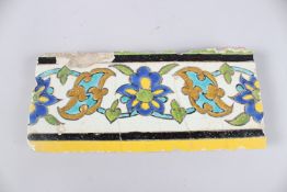 A 17TH CENTURY PERSIAN SAFAVID GLAZED POTTERY CUERDA SECA BORDER TILE. 9.25ins x 4ins.