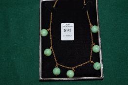 A necklace comprising, seven jade spheres suspended from a yellow metal chain.