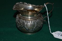 An embossed silver metal milk jug.