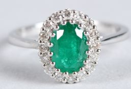 A CERTIFICATED 18CT WHITE GOLD, EMERALD AND DIAMOND CLUSTER RING. Oval-cut emerald 1.18ct. RBC