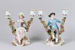 A PAIR OF MEISSEN TWO BRANCH CANDLESTICKS with a gallant and lady sitting on a branch. Crossed sword