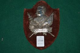 A white metal plaque on velvet shield shaped backing board.