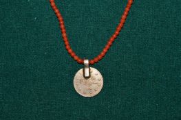 A coral necklace with coin shaped pendant.