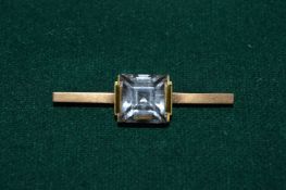 An 18ct gold bar brooch set with a large clear stone.