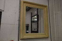 A wall mirror with cream painted frame.