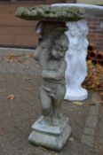 A reconstituted stone bird bath with cherub support.