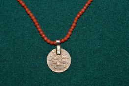 A coral bead necklace with a coin style pendant.