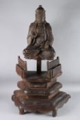 A CARVED WOOD FIGURE OF A BUDDHIST OF DAOIST DEITY sitting cross legged. 30cms high, on a stand.