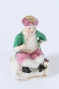 A FIGURE OF A SEATED PORCELAIN TURKISH MAN SITTING GROSS-LEGGED ON A CUSHION. 10cms high.