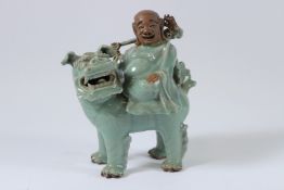 A POTTERY FIGURE OF A MAN riding on a foo dog. 26cms high.