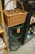 A wicker bottle carrier and green painted wrought iron four tier vegetable stand.