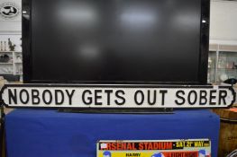 A novelty carved wood and painted sign 'Nobody gets out sober'.