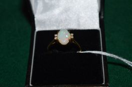 A yellow metal ring set with an oval opal, flanked by small diamonds.