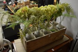 A wooden box containing ten glass bottles with artificial plants.