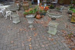 A pair of reconstituted stone classical style garden urns on pedestal stands.