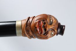 A 19TH CENTURY WALKING STICK with a carved wood clown handle. 90cms long.