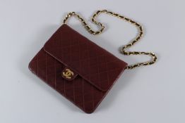 A CHANEL BURGUNDY PADDED LEATHER BAG with gilt double C, gilt and leather strap. 22cms long, with