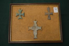 Three bronze crucifixes on a framed mount.