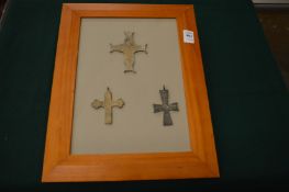 Three bronze crucifixes on a framed mount.
